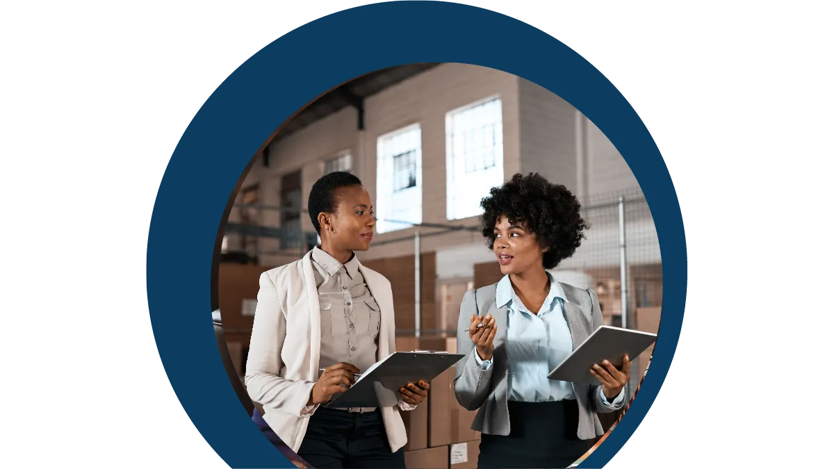 Two professionals holding tablets in conversation in a warehouse