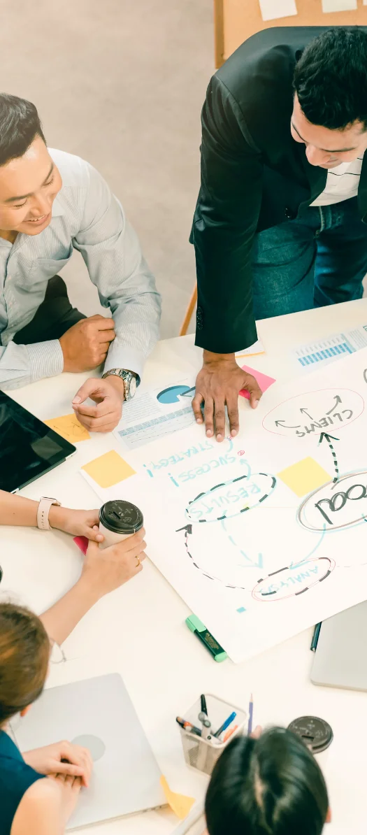 Overhead view of a team around a table with a hand-drawn goal and strategy diagram, sticky notes and laptops