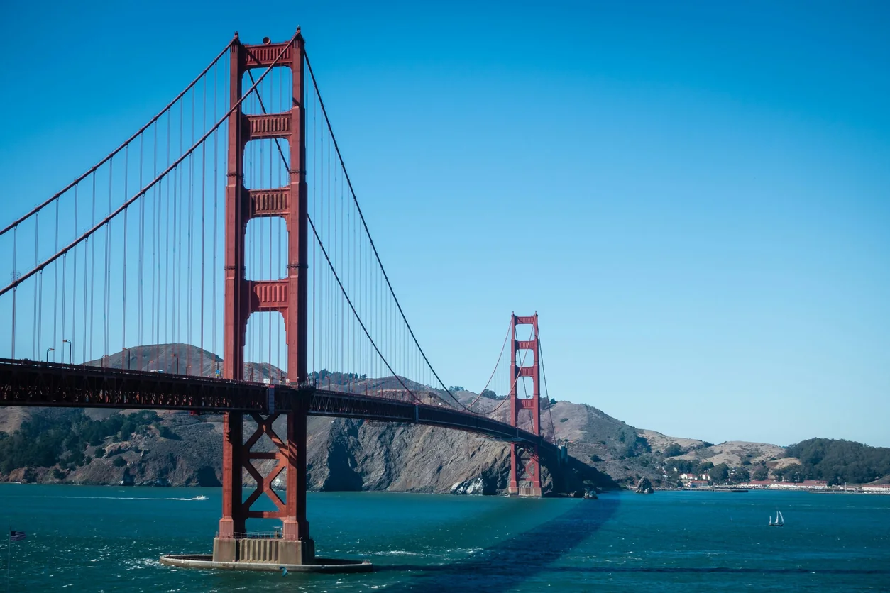 Golden Gate Bridge over blue water with hills behind under a clear sky