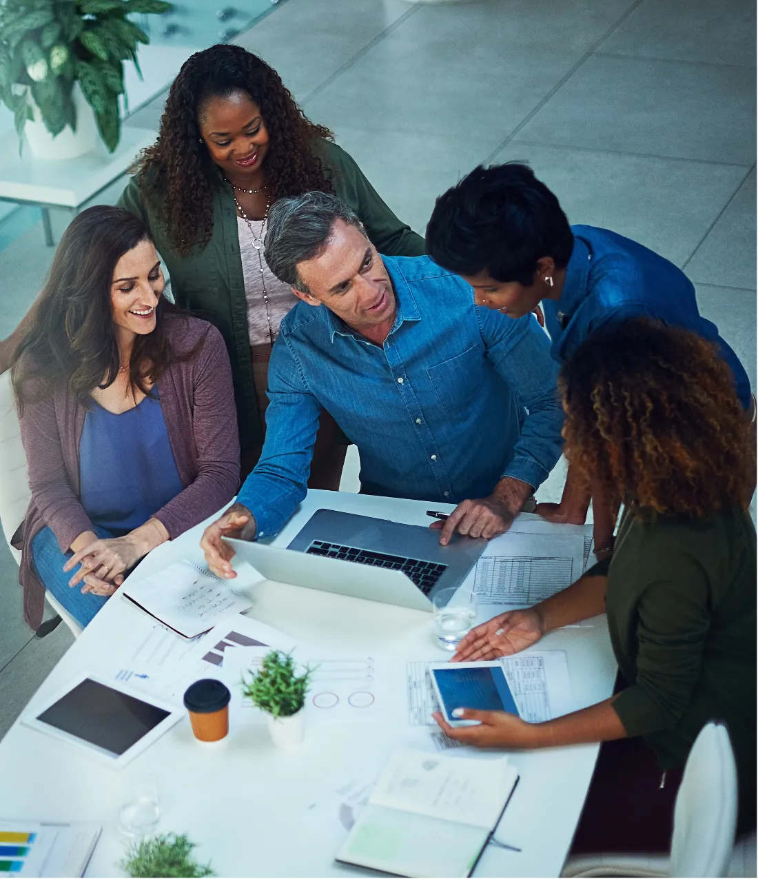 Five colleagues gathered around a laptop and papers on a white table in an office