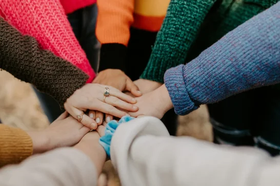 Hands stacked together in a circle, arms in colorful knit sweaters