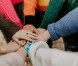 Hands stacked together in a circle, arms in colorful knit sweaters