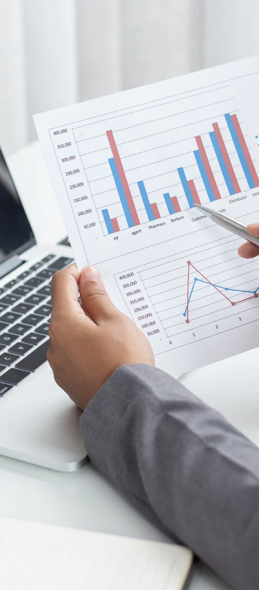 Hand holding a printed page of bar and line charts beside a laptop